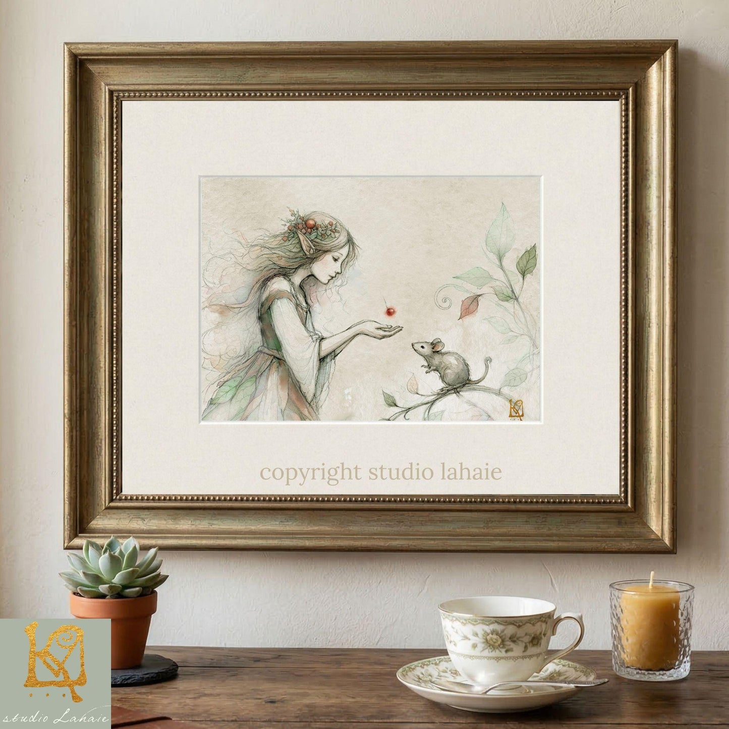 a framed illustration of a woman with a mouse on a branch, accompanied by a teacup and a candle on a wooden table.