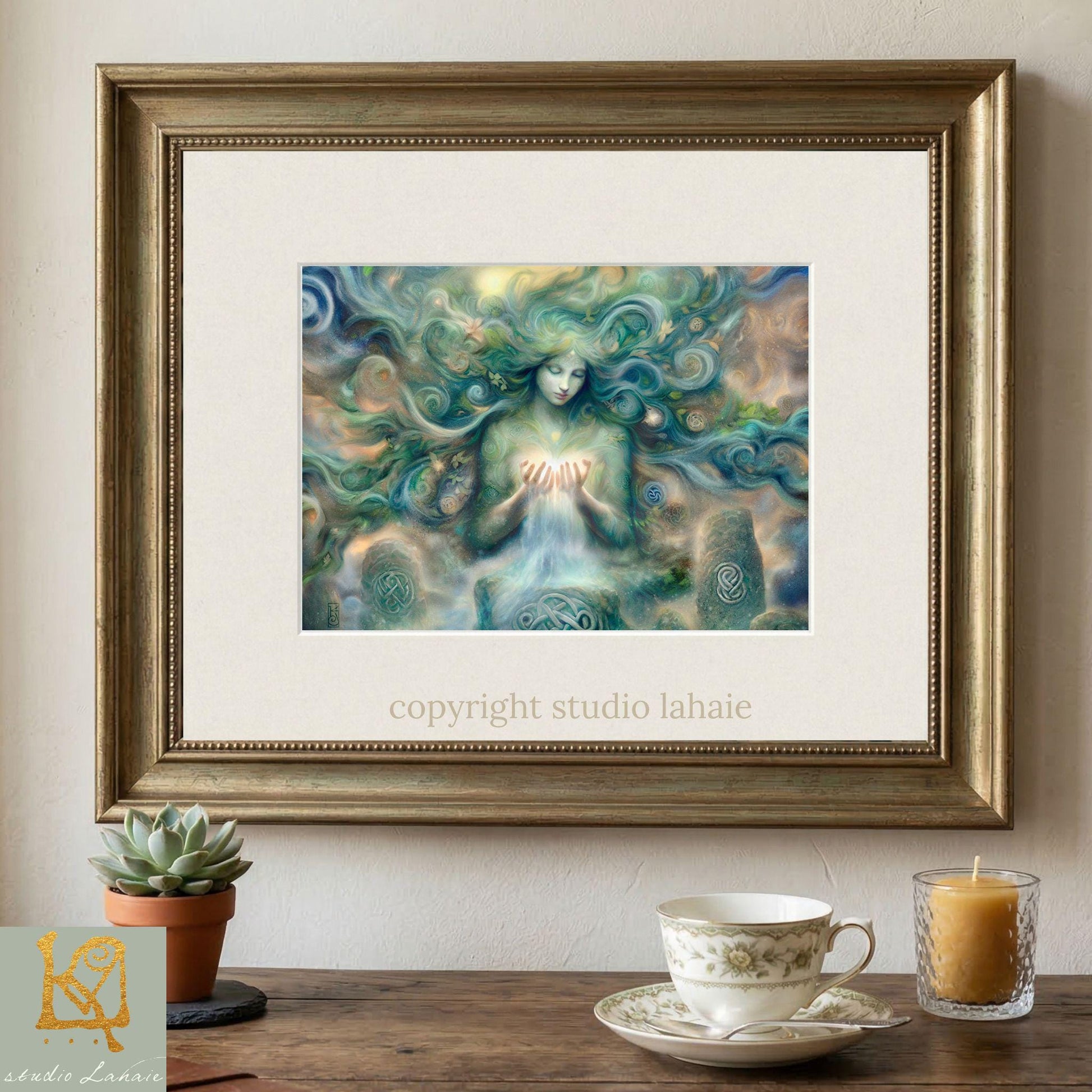 a framed painting of a woman with flowing hair and a green, ethereal appearance, displayed on a wall above a wooden table with a teacup and a candle.